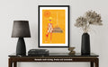 Framed artwork of a stylized figure on a table with decor items.