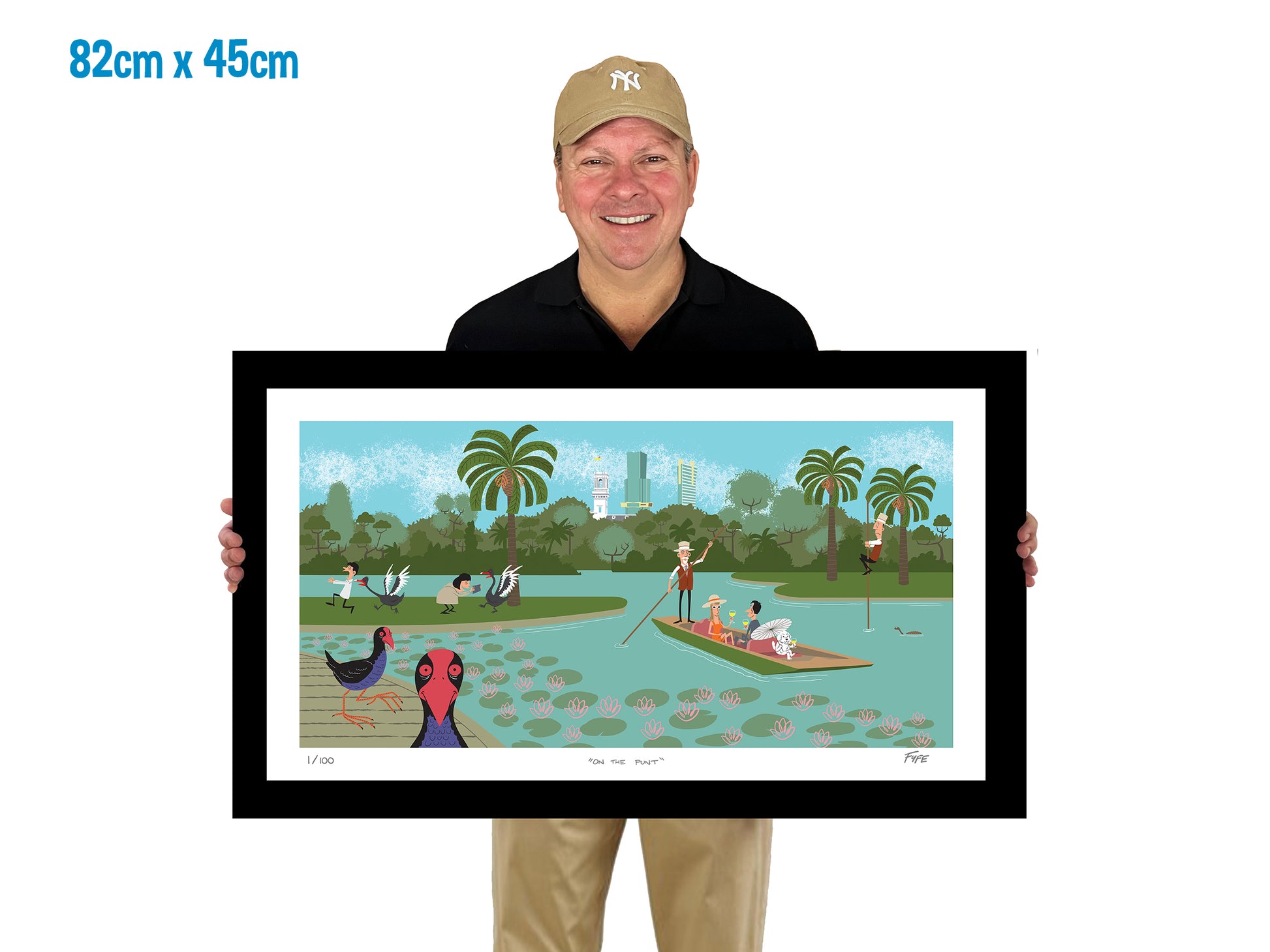 Man holding a framed artwork of a park scene with people and animals.