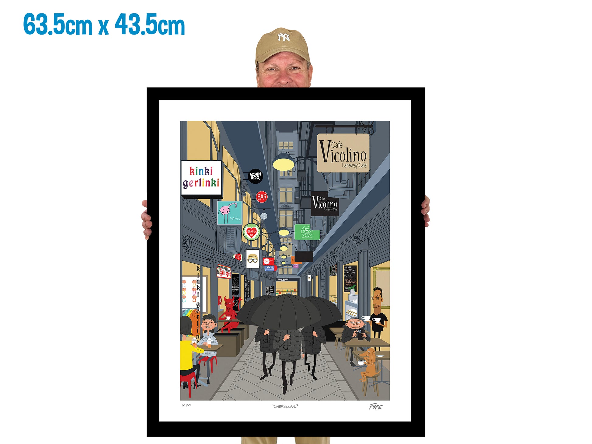Person holding a framed illustration of a city street scene with various shops and people.