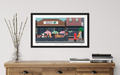 Framed artwork of a city street scene on a wooden sideboard with decorative items.
