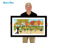 Man holding a framed artwork of a park scene with people and trees.