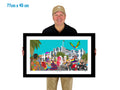Man holding a framed artwork of a colorful scene with people and buildings.