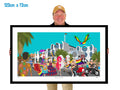 Person holding a large framed artwork of a colorful scene with people and buildings.