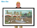 Person holding a framed artwork of a cityscape with people and vehicles.