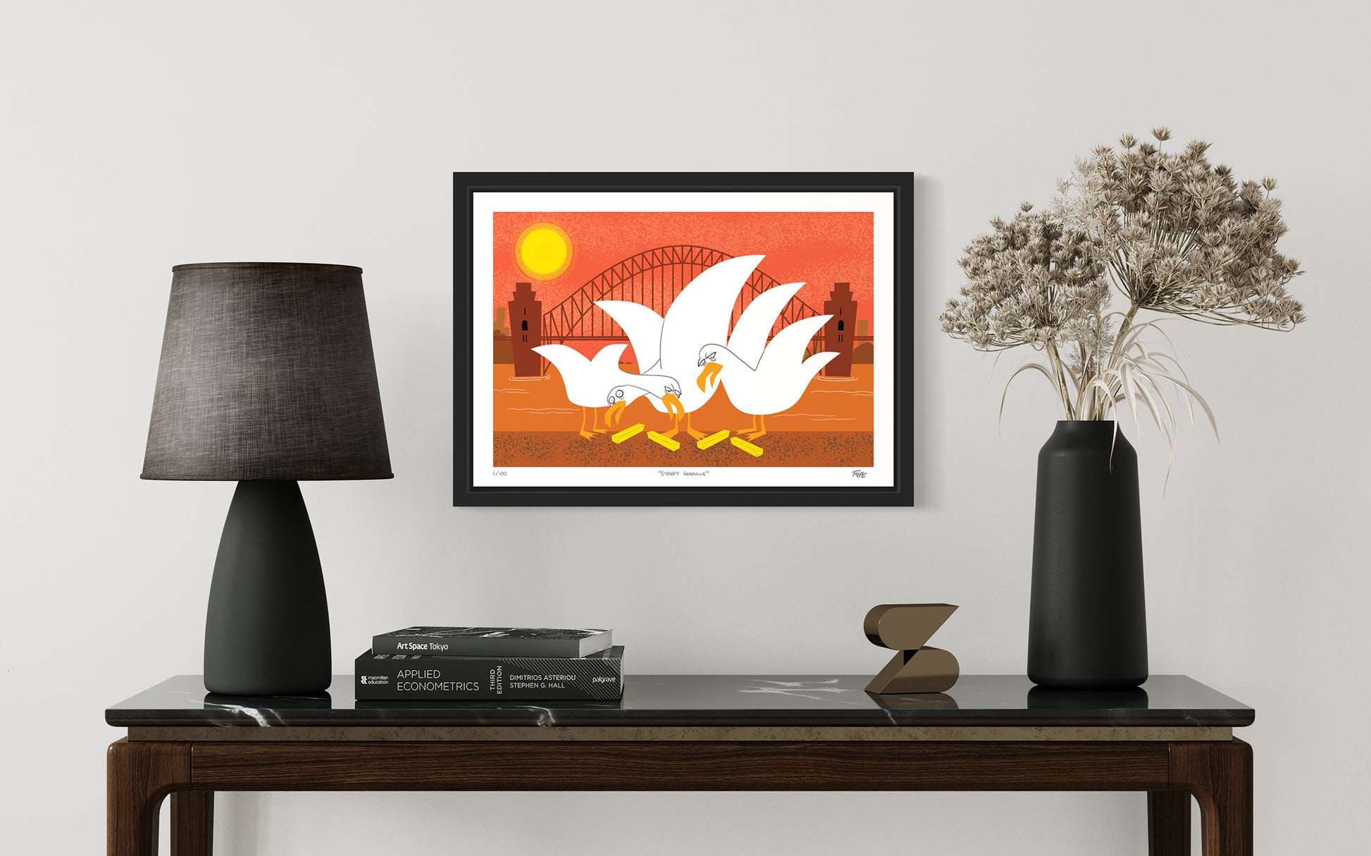 Framed artwork of two birds on an orange background above a table with decor items.