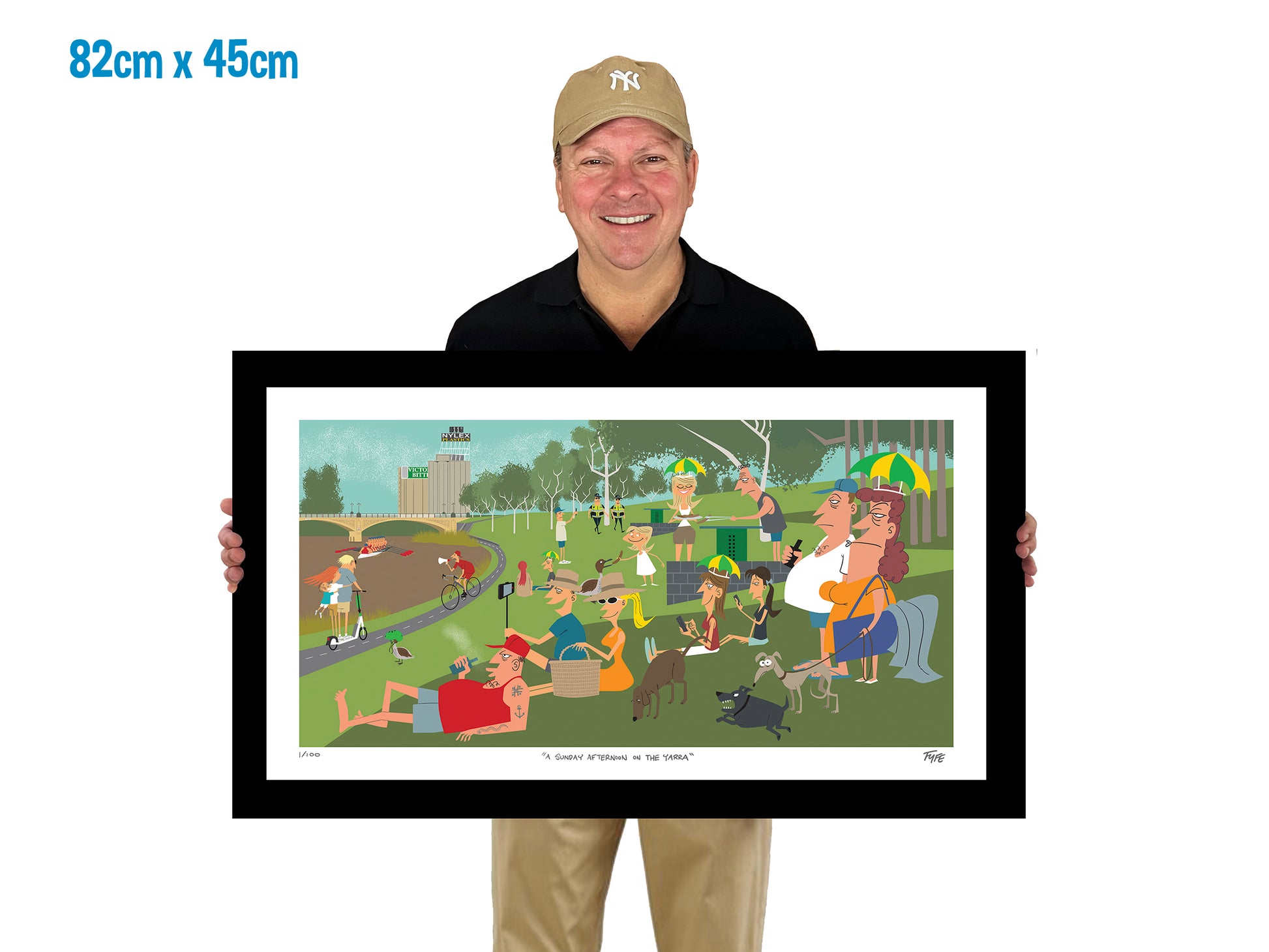 Man holding a framed artwork of a park scene with people and dogs.